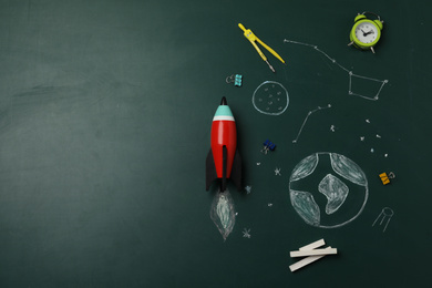 Bright toy rocket, school supplies and drawings on chalkboard, flat lay. Space for text