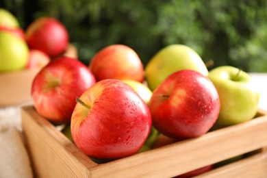 Fresh ripe apples in wooden crate on blurred background, closeup