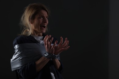 Scared woman taped up and taken hostage on dark background. Space for text
