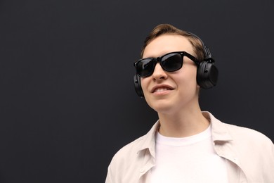 Handsome young man with headphones near black wall. Space for text
