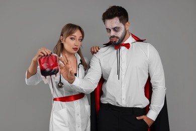 Photo of Couple in scary nurse and vampire costumes with blood bag on light grey background. Halloween celebration