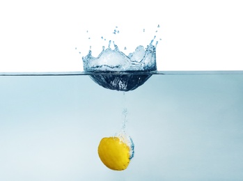 Photo of Ripe lemon falling down into clear water with splashes against beige background