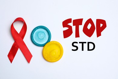Colorful condoms, red ribbon and text STOP STD on white background, flat lay