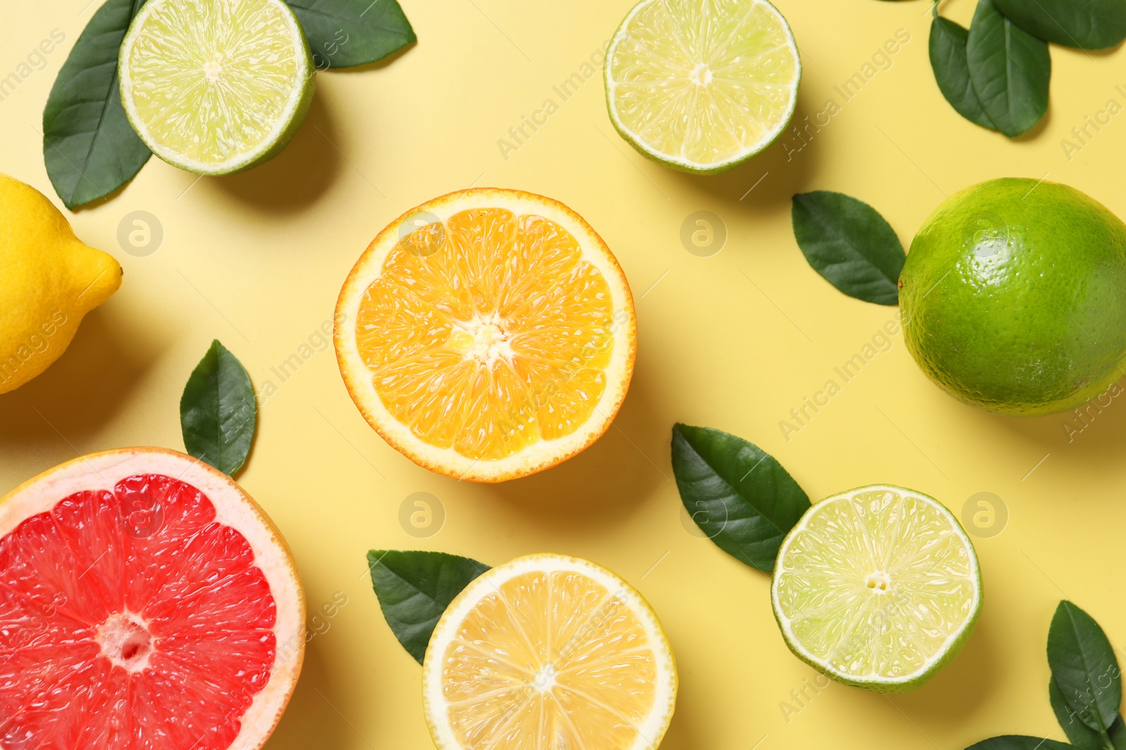 Photo of Different cut and whole citrus fruits on yellow table, flat lay