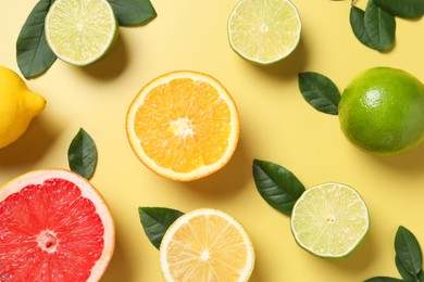 Different cut and whole citrus fruits on yellow table, flat lay