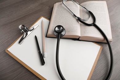 Book, stethoscope and stationery on wooden table, above view. Medical education