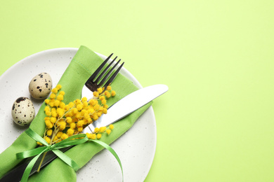 Photo of Festive Easter table setting with quail eggs and floral decor on green background, top view. Space for text