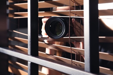 Photo of Private detective with camera spying near window indoors, closeup