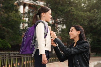 Photo of Happy mother helping her little daughter to zipper jacket before school outdoors
