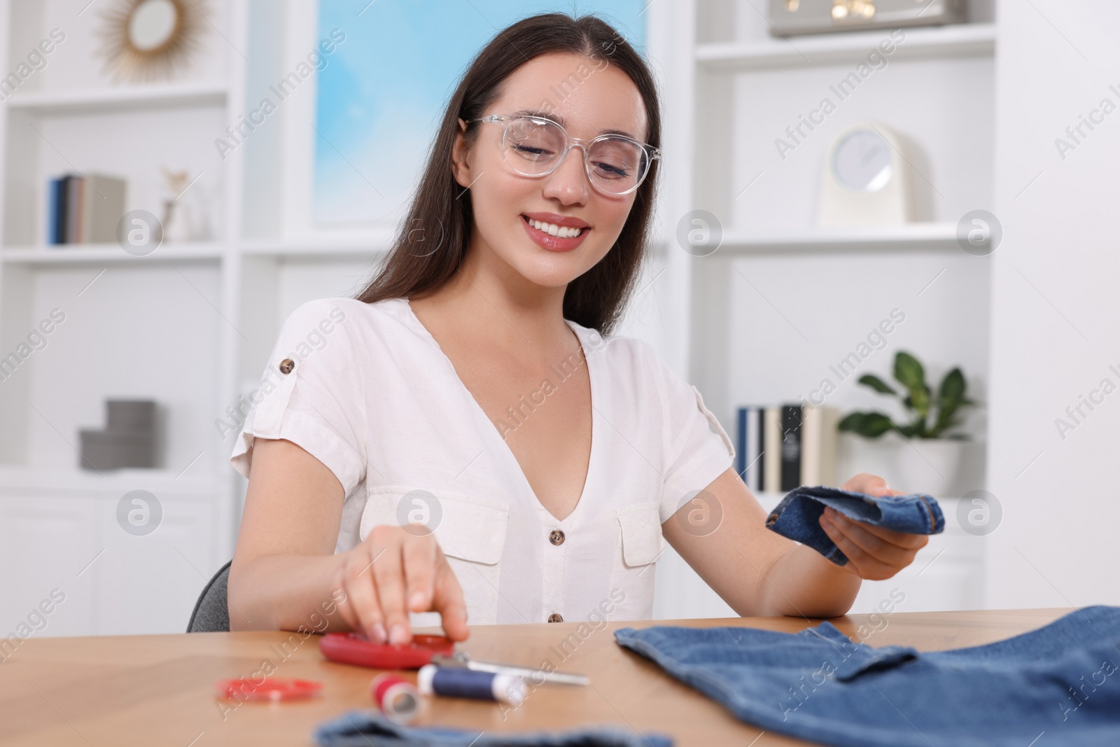 Photo of Happy woman holding cut hem and jeans at table indoors