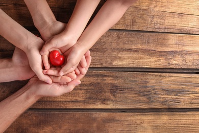 Photo of Family holding small red heart in hands on wooden background