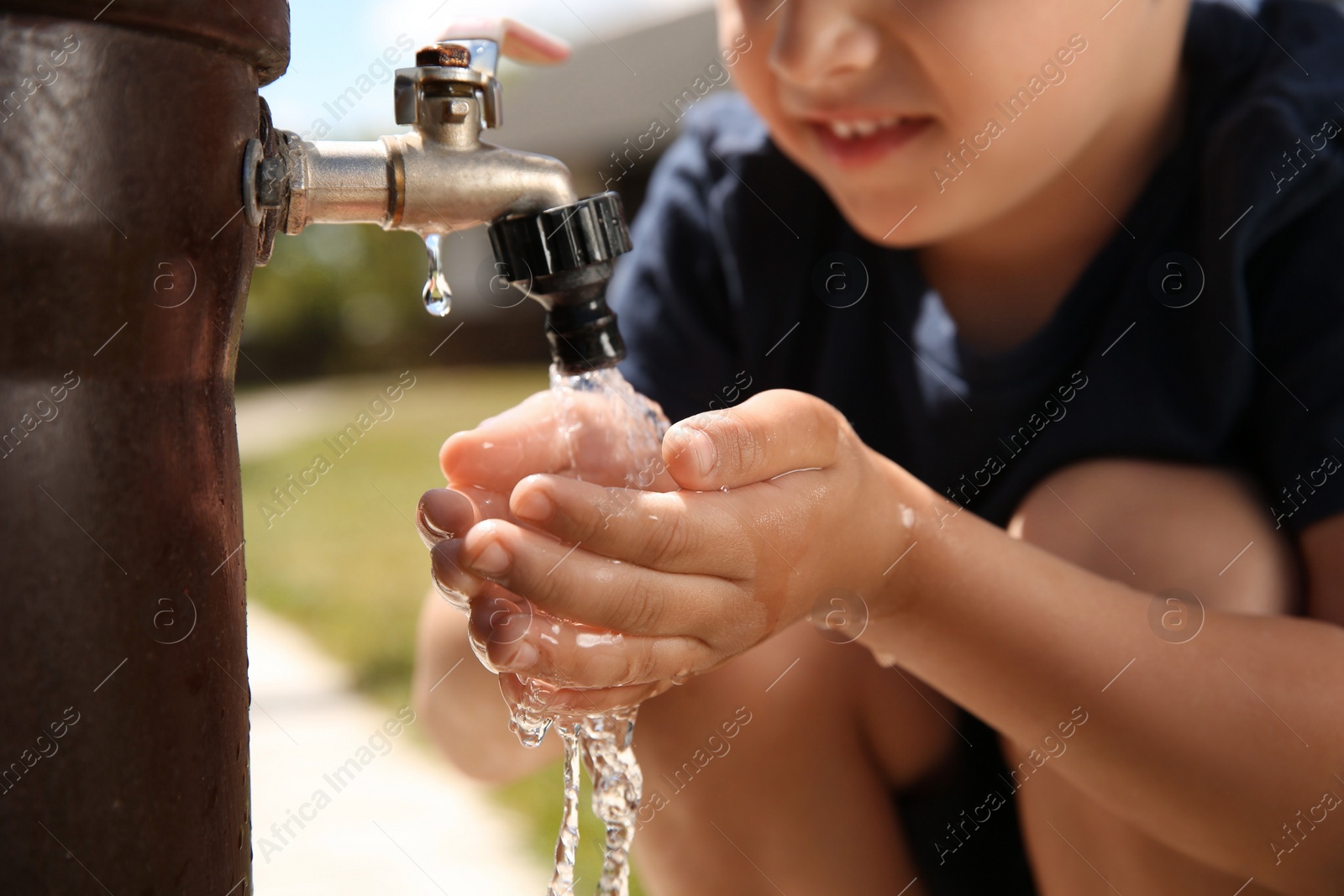 Photo of Water scarcity. Little boy drinking water from tap outdoors, closeup