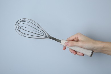 Woman holding metal whisk on light grey background, closeup