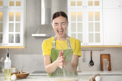 Photo of Funny woman clapping floury hands over messy table in kitchen
