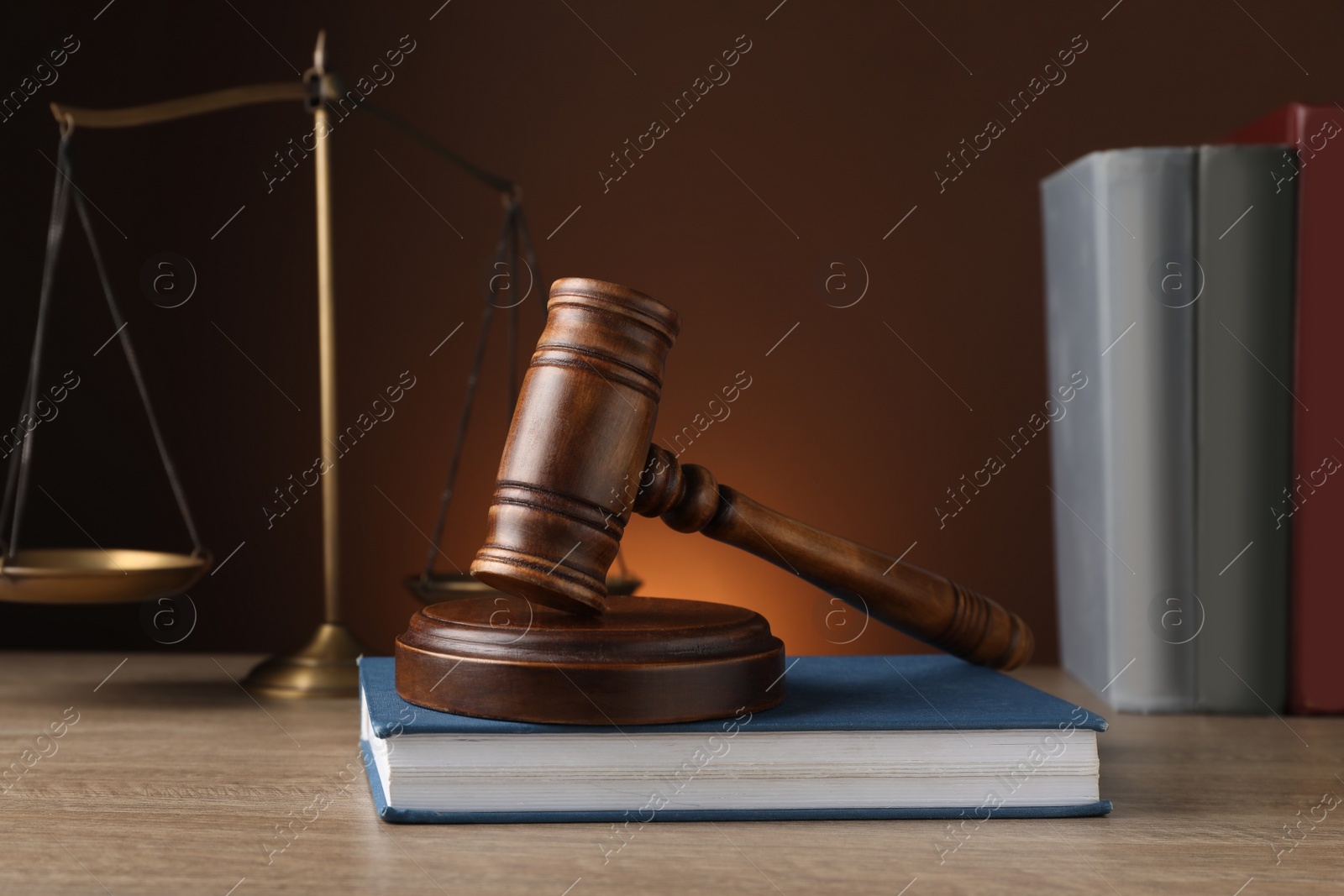 Photo of Judge's gavel with sound block, scales of justice and books on wooden table against brown background