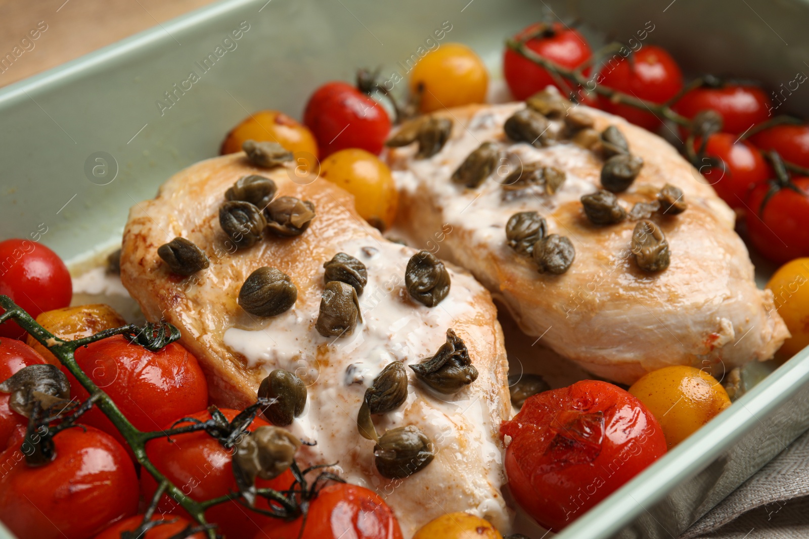 Photo of Delicious chicken fillets with capers, tomatoes and sauce in baking dish, closeup