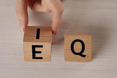 Woman turning cube with letters E and I near Q at white wooden table, top view