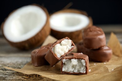 Photo of Delicious milk chocolate candy bars with coconut filling on wooden table, closeup. Space for text