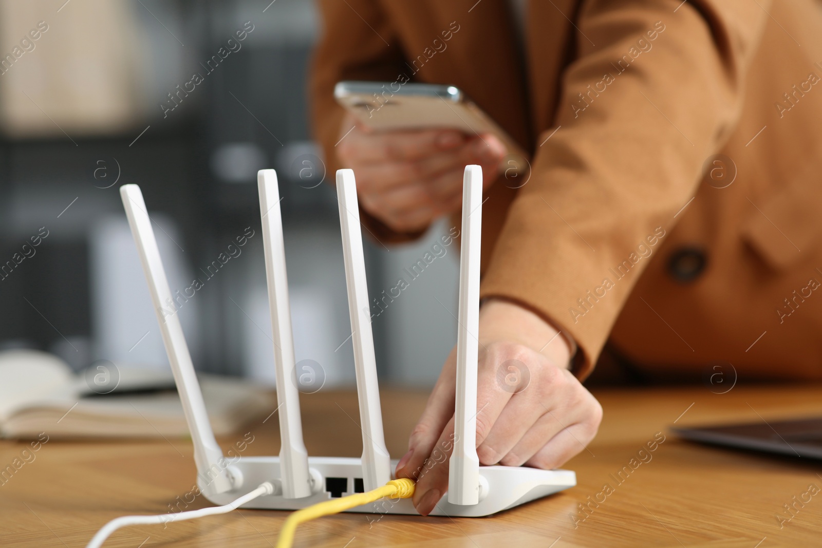 Photo of Woman with smartphone connecting cable to Wi-Fi router at table indoors, closeup