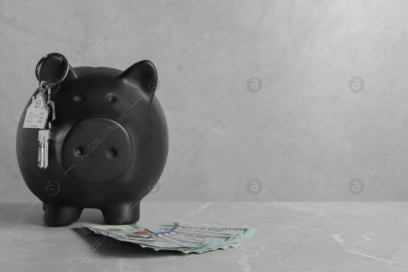 Photo of Piggy bank, dollar banknotes and house keys on grey marble table. Space for text