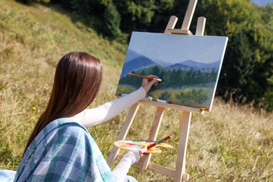 Photo of Young woman drawing on easel with brush outdoors