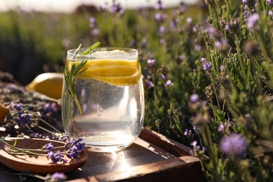 Photo of Glass of fresh lemonade on wooden tray in lavender field. Space for text