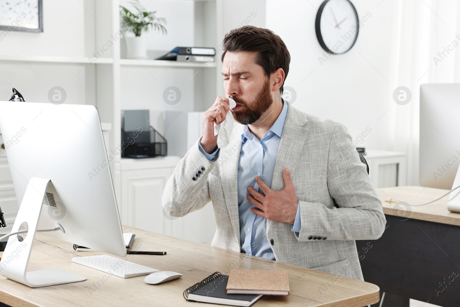 Photo of Sick man with tissue coughing at workplace in office