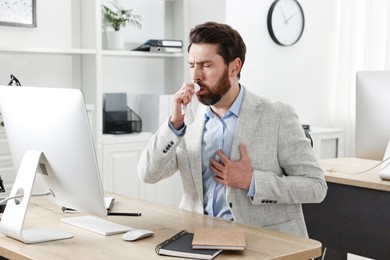 Sick man with tissue coughing at workplace in office