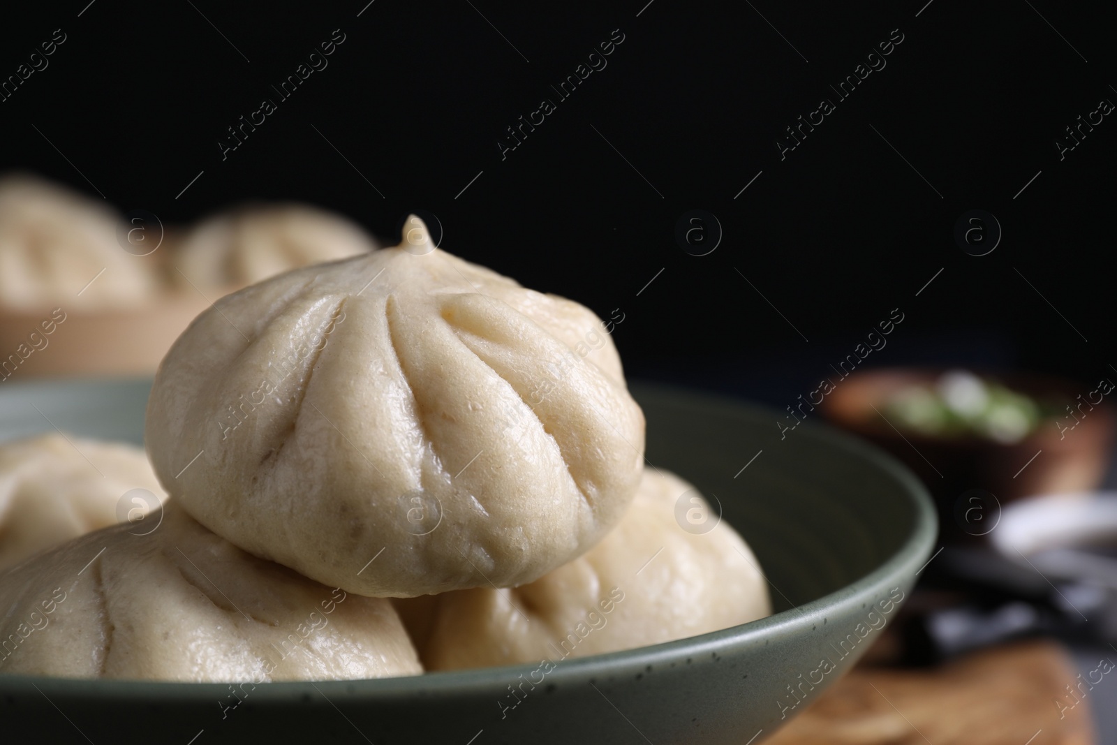 Photo of Delicious bao buns (baozi) in bowl on blurred background, closeup