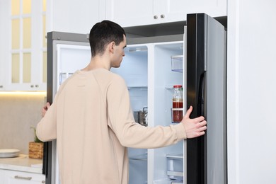 Man near open refrigerator in kitchen at home