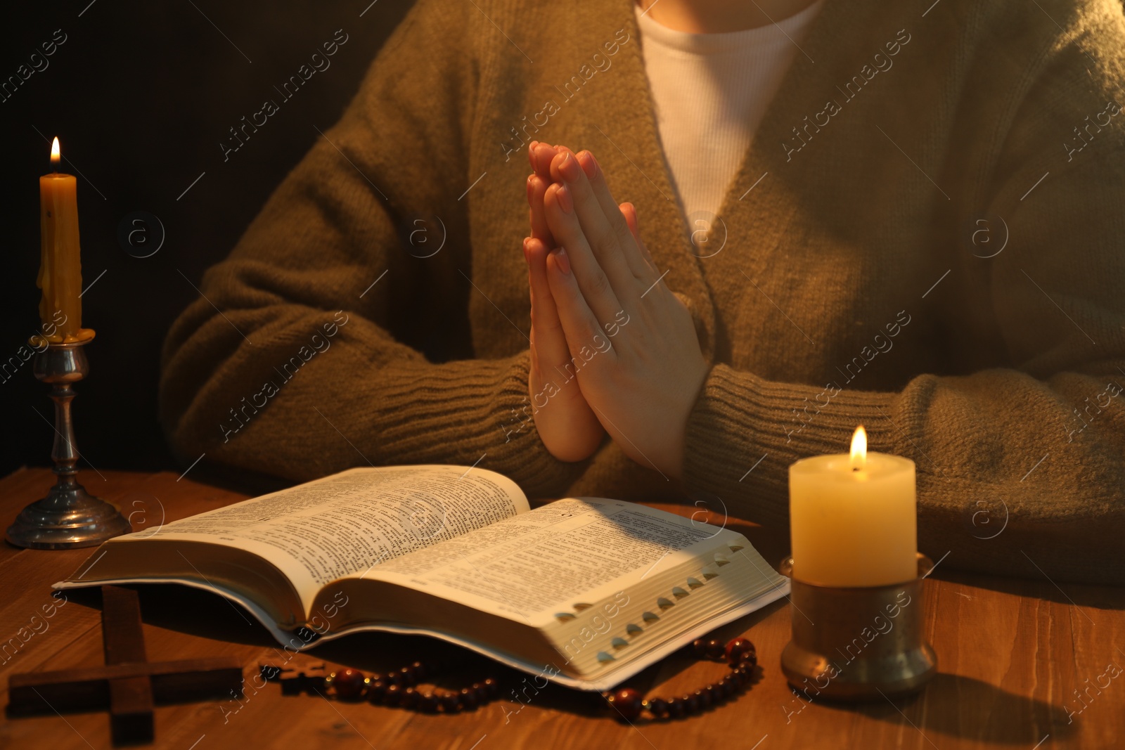 Photo of Woman praying at table with burning candles and Bible, closeup