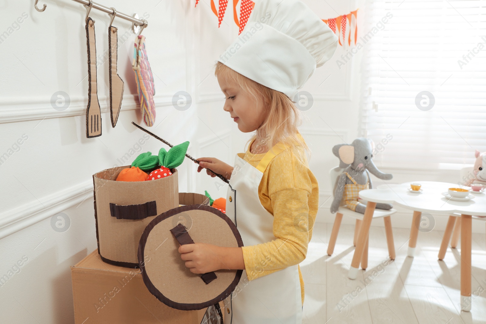 Photo of Little girl playing with toy cardboard kitchen at home