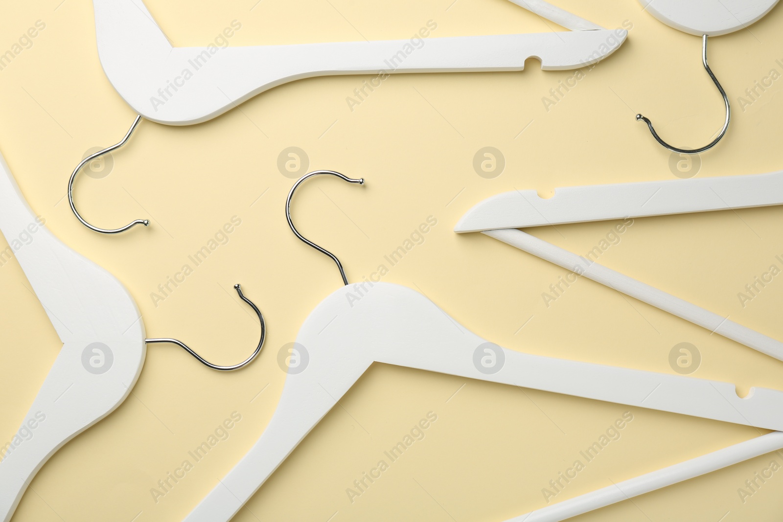 Photo of White hangers on pale yellow background, flat lay