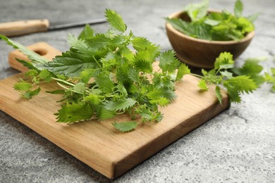 Photo of Wooden board with fresh stinging nettle leaves on grey table, closeup
