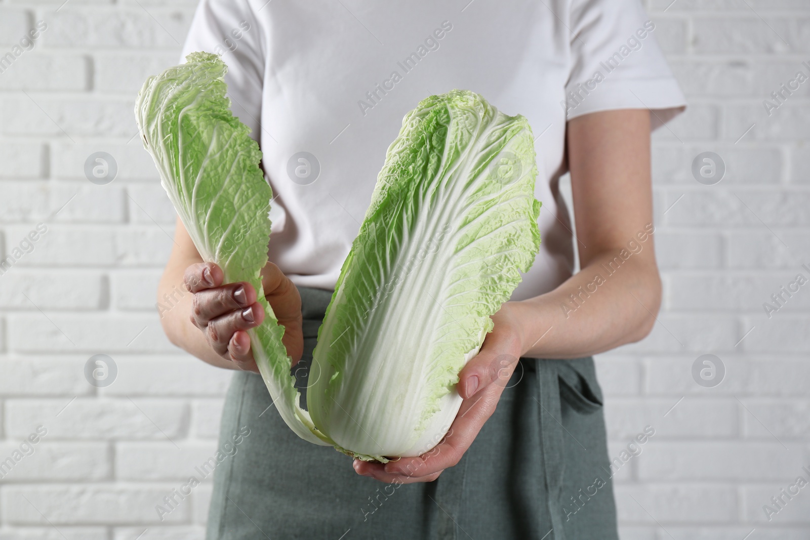 Photo of Woman separating leaf from fresh Chinese cabbage near white brick wall, closeup