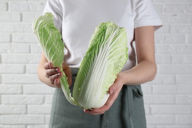 Photo of Woman separating leaf from fresh Chinese cabbage near white brick wall, closeup