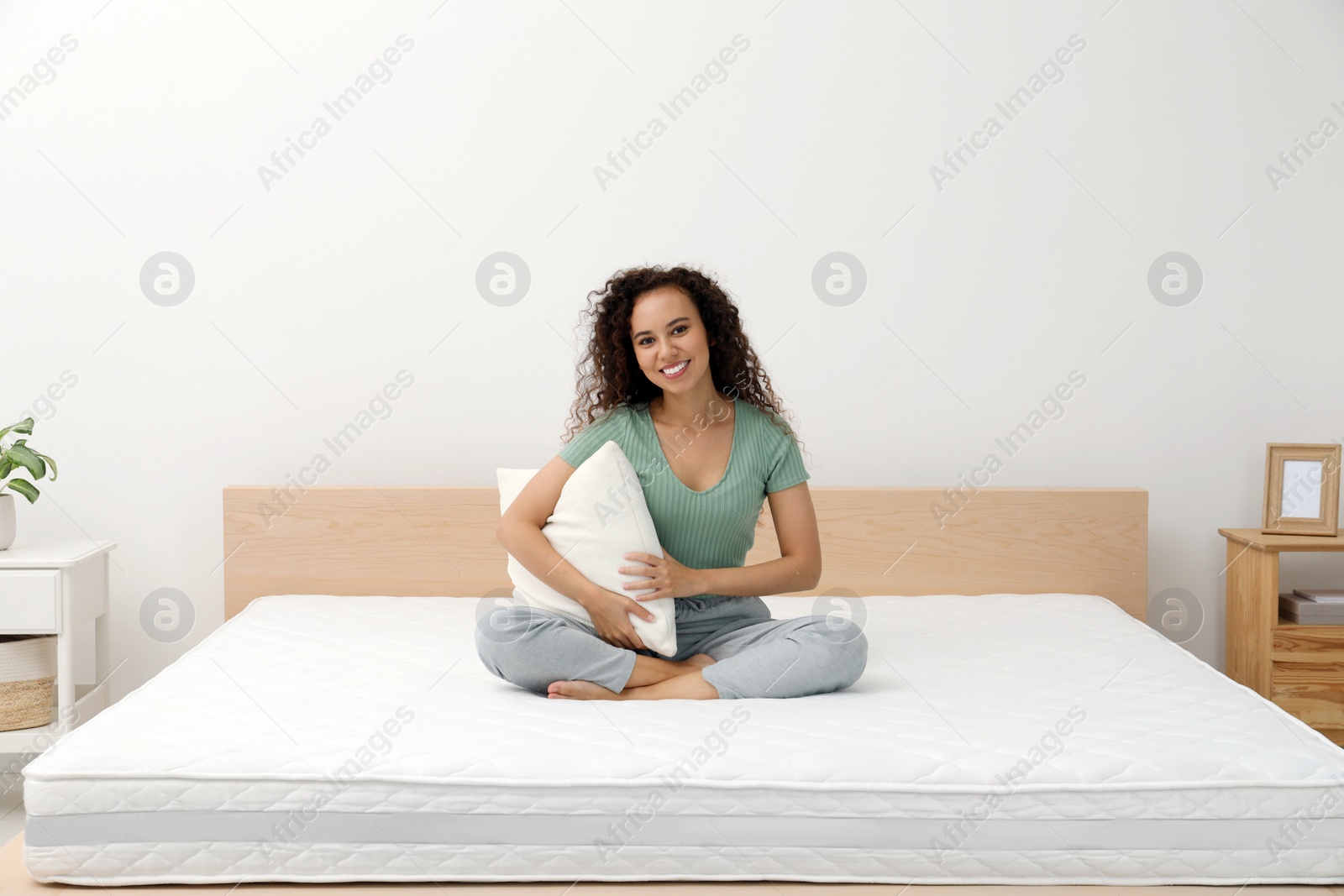 Photo of Happy young African American woman holding pillow on bed with comfortable mattress at home