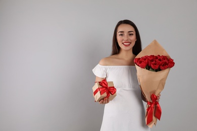 Happy woman with red tulip bouquet and gift box on light grey background, space for text. 8th of March celebration