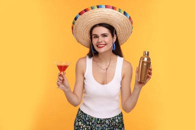 Photo of Young woman in Mexican sombrero hat with cocktail and shaker on yellow background