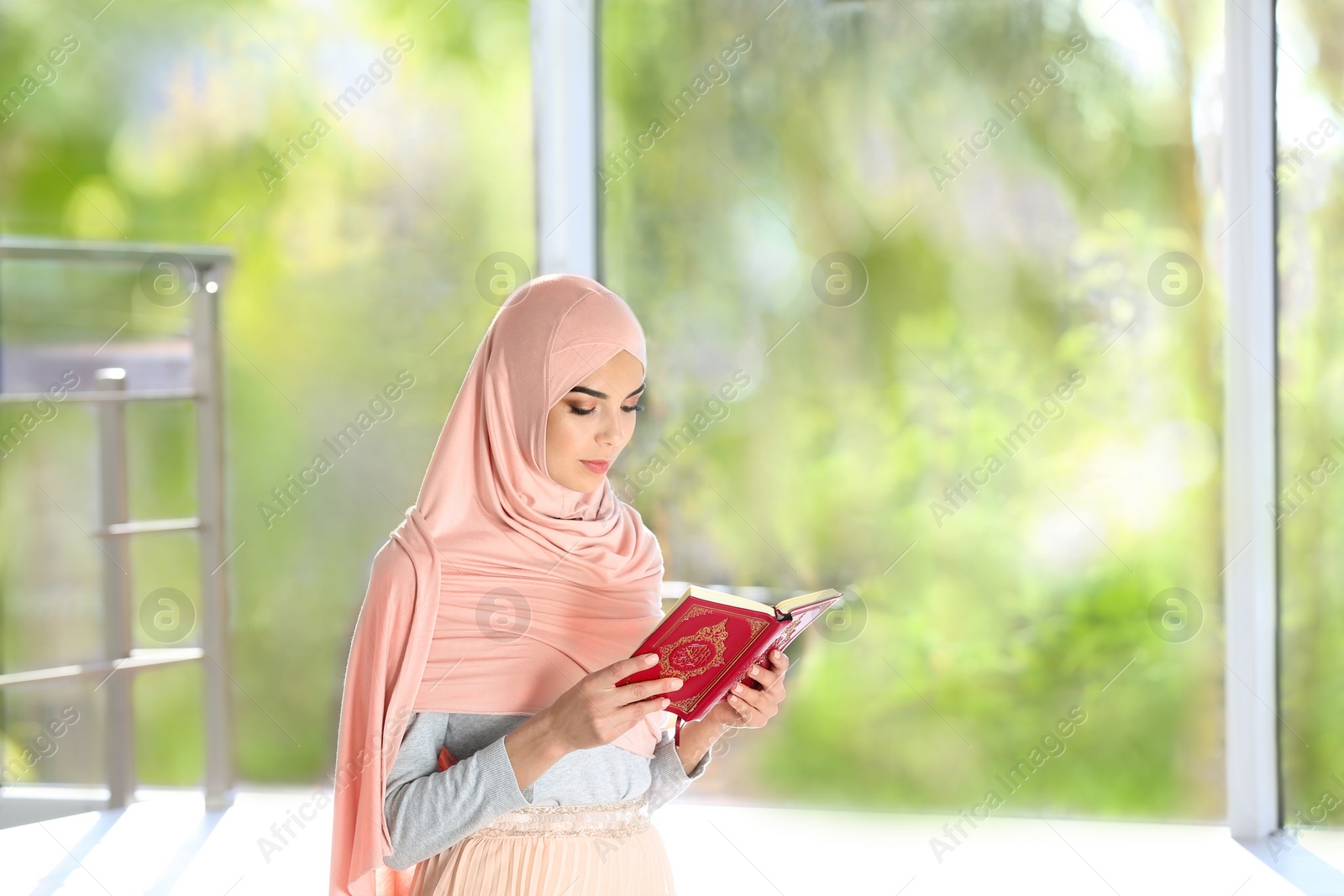 Photo of Muslim woman in hijab reading Koran indoors