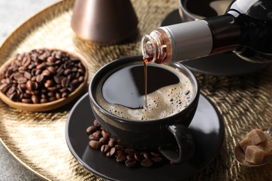 Photo of Pouring syrup into cup of tasty coffee on grey table, closeup