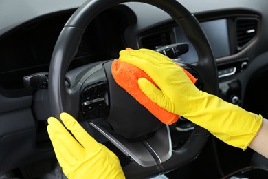 Photo of Woman cleaning steering wheel with rag in car, closeup