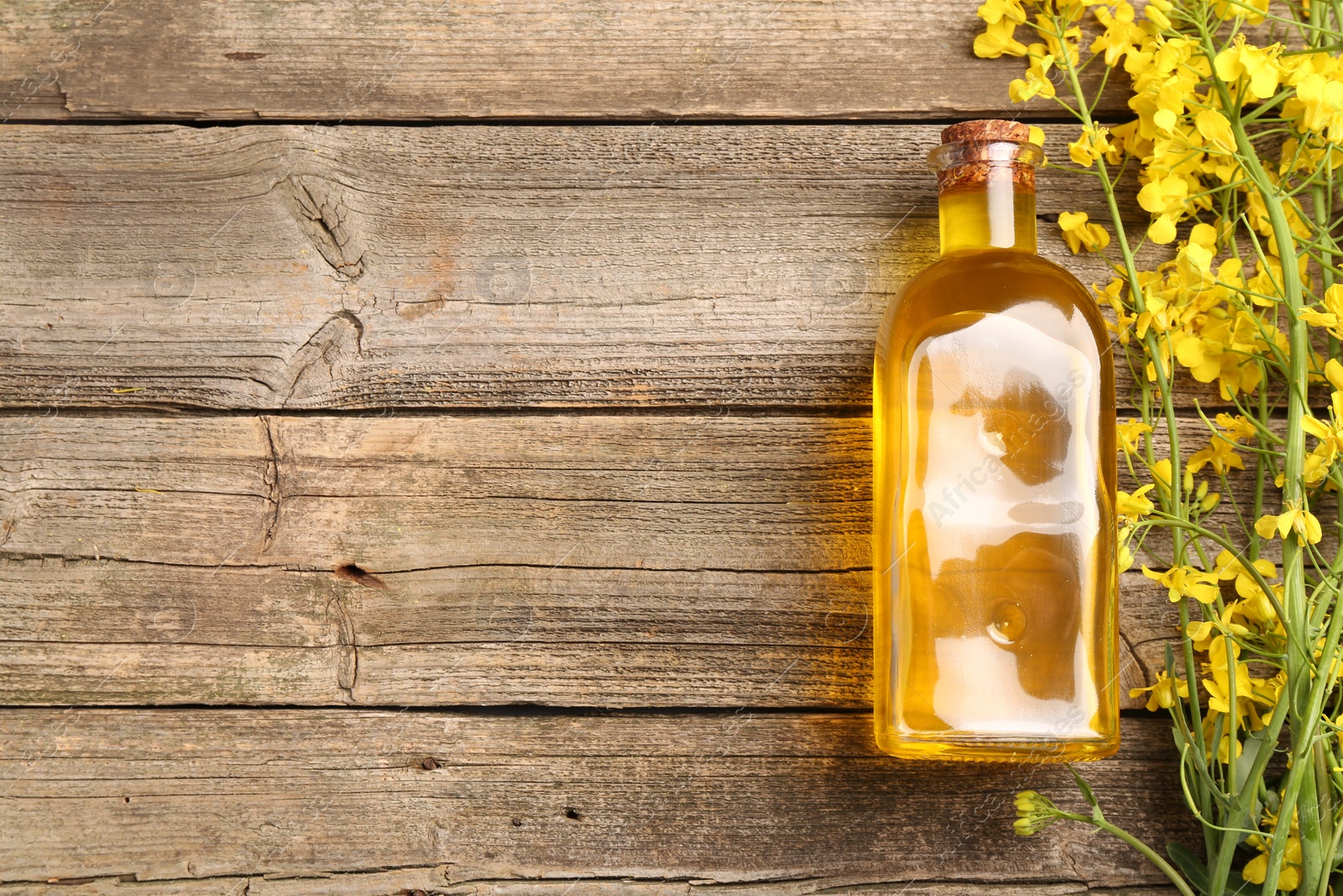 Photo of Rapeseed oil in glass bottle and beautiful yellow flowers on wooden table, flat lay. Space for text