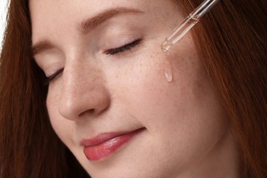 Beautiful woman with freckles applying cosmetic serum onto her face, closeup