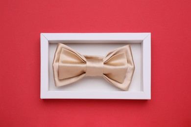 Stylish beige bow tie in box on red background, top view