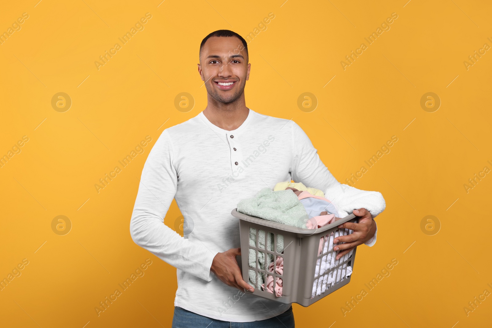 Photo of Happy man with basket full of laundry on orange background