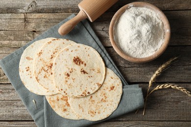 Photo of Tasty homemade tortillas, flour, rolling pin and spikes on wooden table, top view
