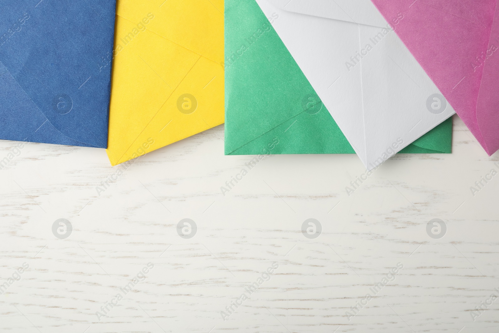 Photo of Colorful paper envelopes on white wooden background, flat lay. Space for text