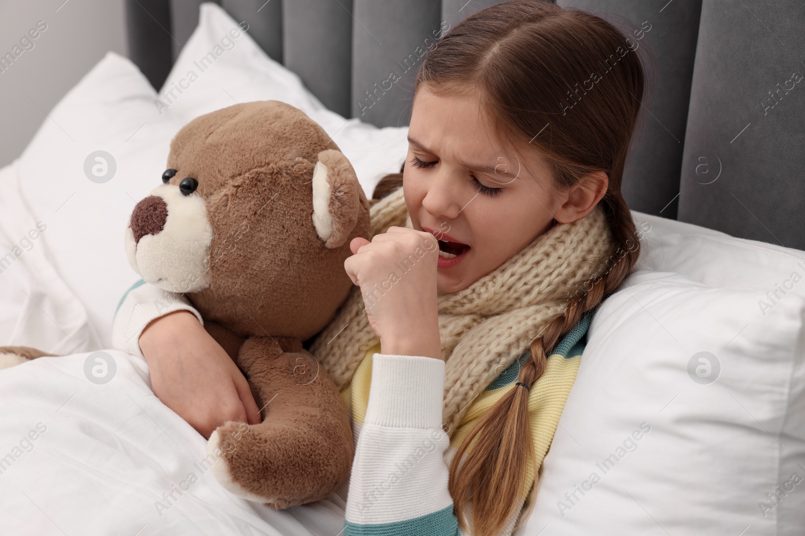 Photo of Sick girl with teddy bear coughing on bed at home