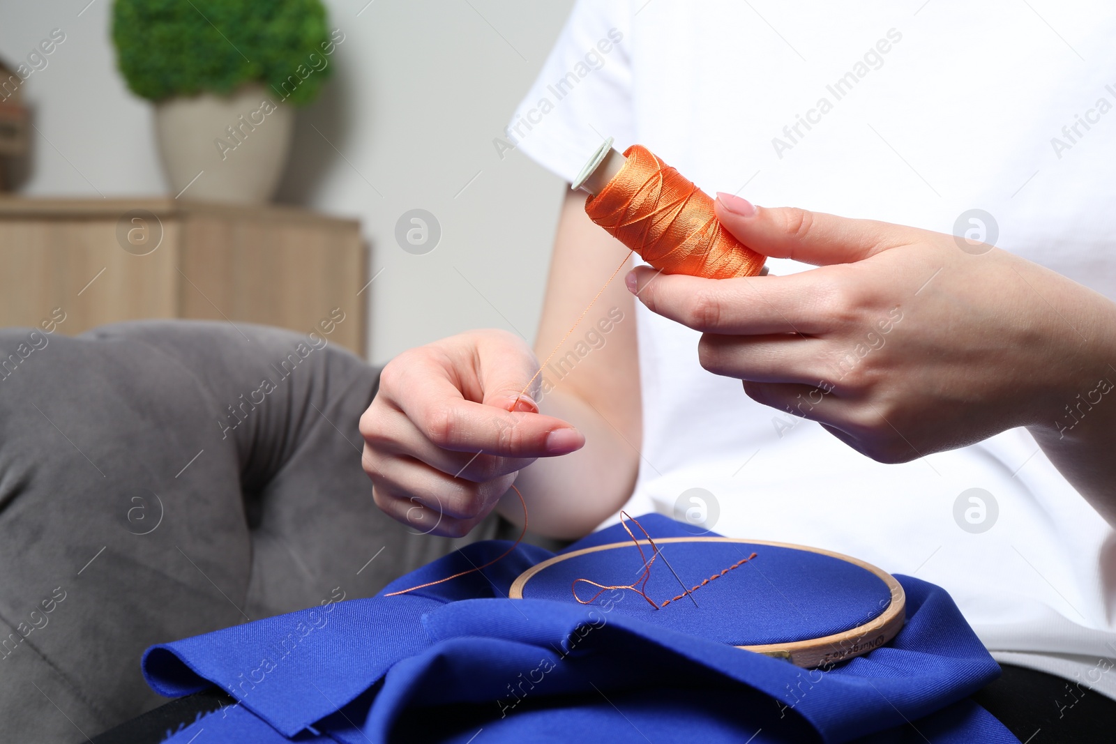 Photo of Woman with spool of thread embroidering on cloth at home, closeup